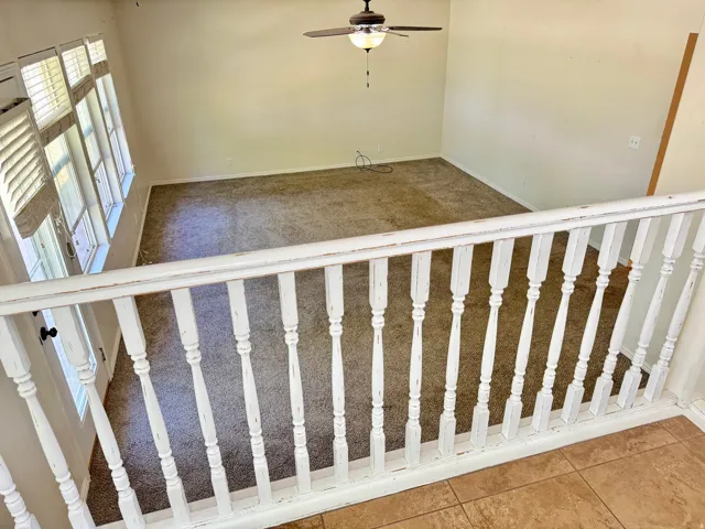 Loft area overlooking a carpeted room featuring a ceiling fan with light, multiple windows, and white plantation shutters