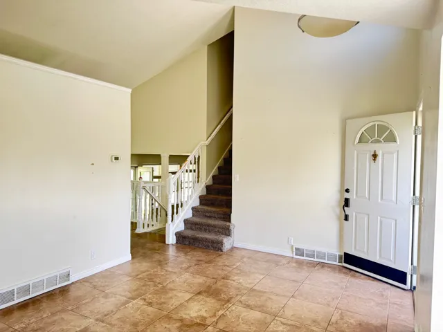 Entry foyer featuring neutral-toned tile flooring, a white paneled entry door with an arched transom, and a carpeted staircase with white railings