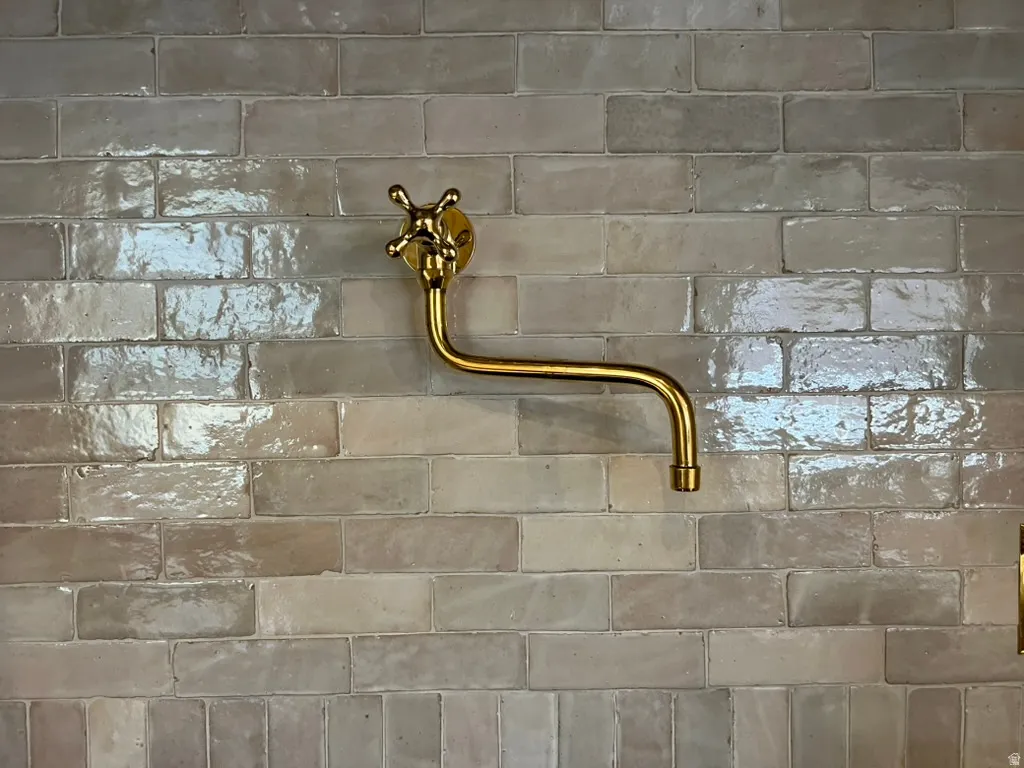 Wall-mounted brass fixture with cross-handle and a long, curved spout set against light-toned subway tile with a glossy finish