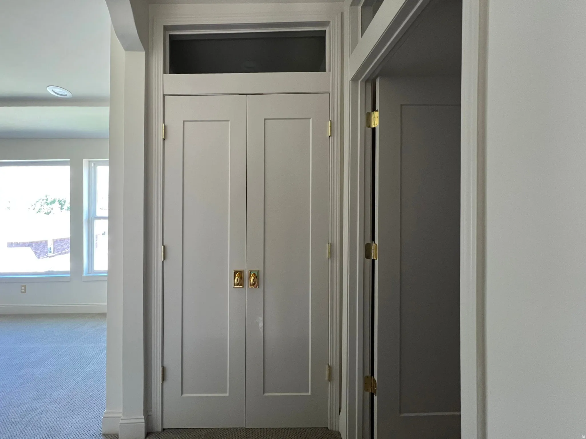 Light gray double doors with brass hardware, featuring a transom window above