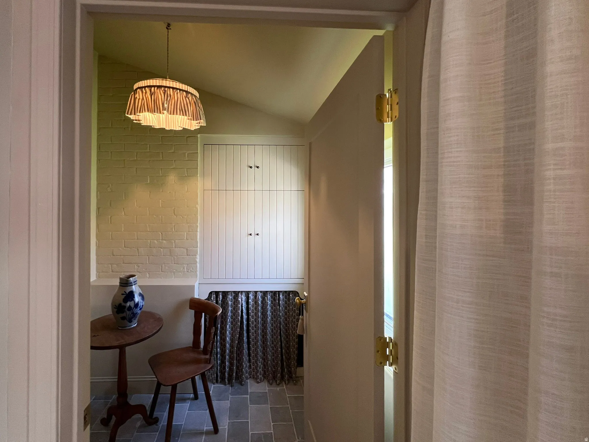 Entryway featuring a vaulted ceiling with a decorative pendant light, painted brick wall, built-in cabinetry, and stone tile flooring