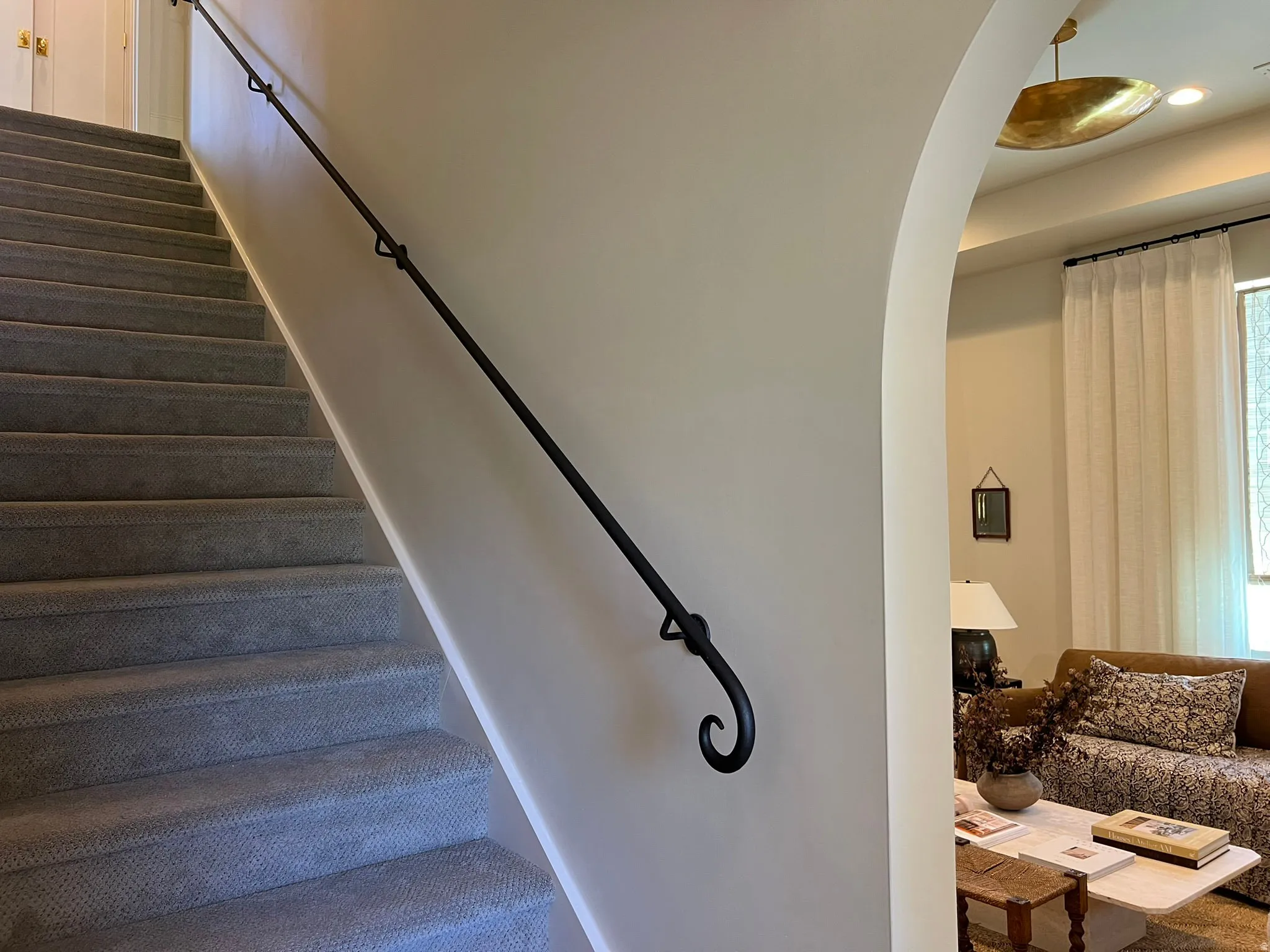 Carpeted staircase with a wrought iron handrail featuring decorative scrolled end
