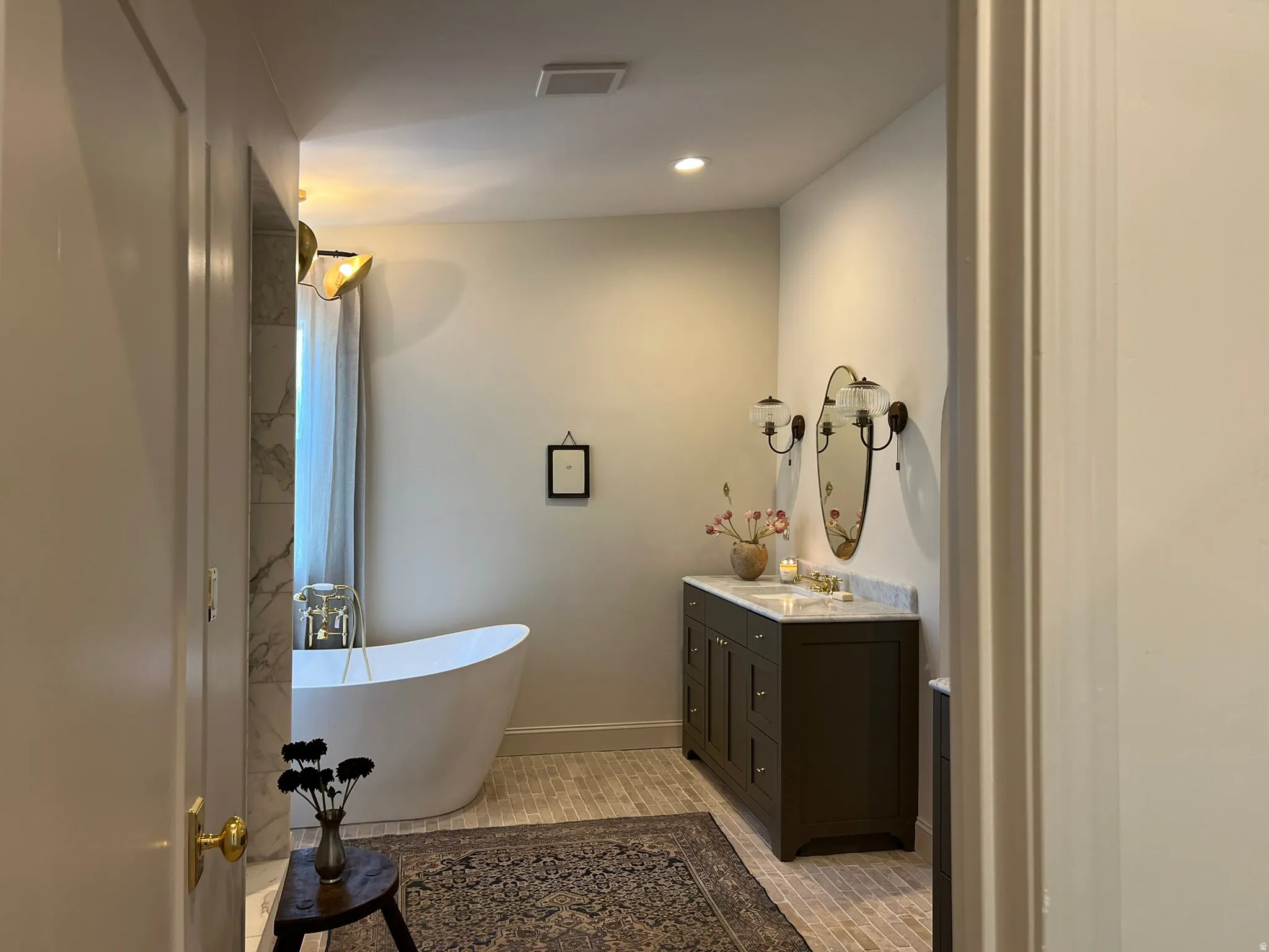 Bathroom featuring a freestanding soaking tub, dual vanity with a stone countertop, sconce lighting, and subway tile flooring