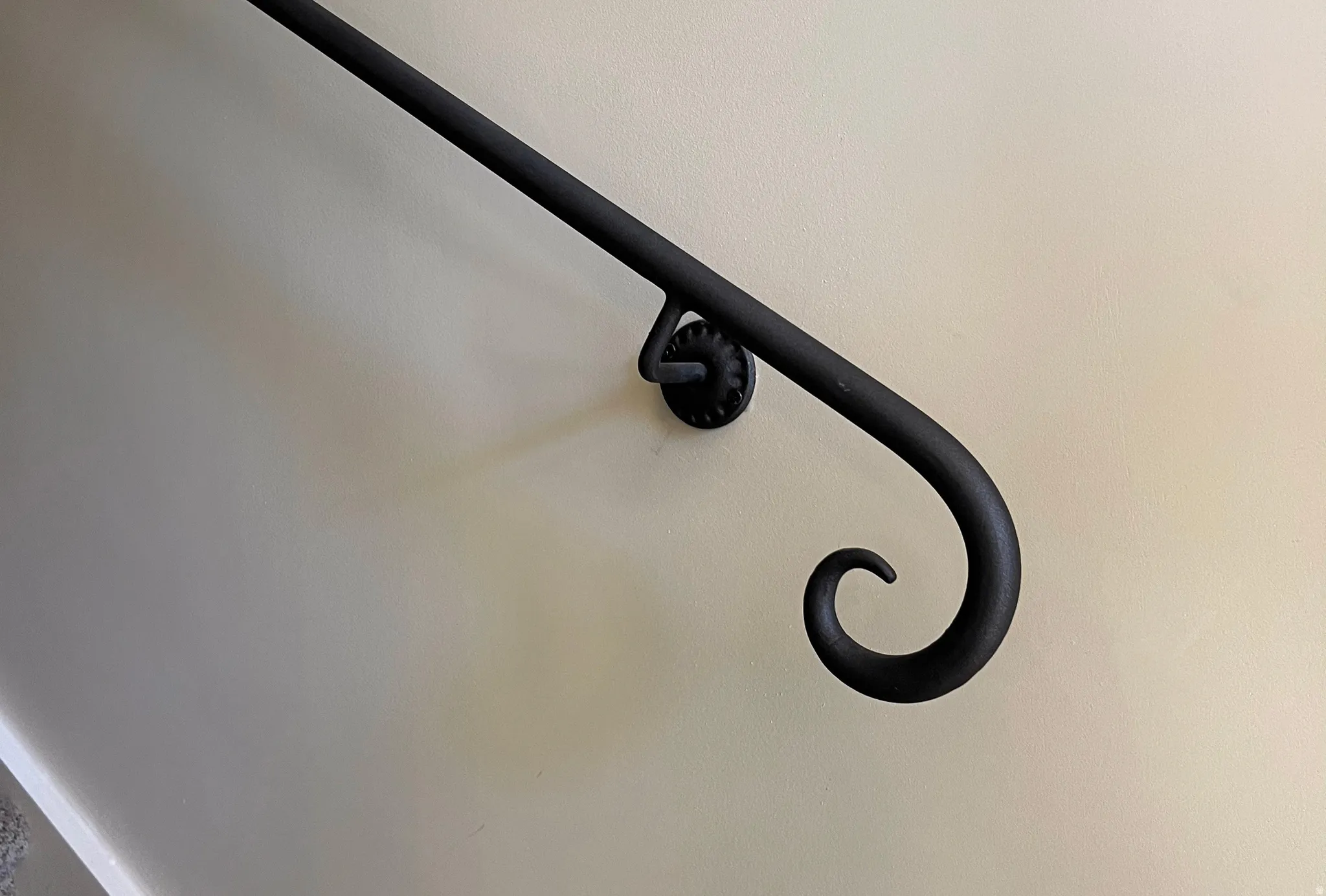 Wrought iron handrail with an ornate scroll detail, mounted on a neutral-toned wall