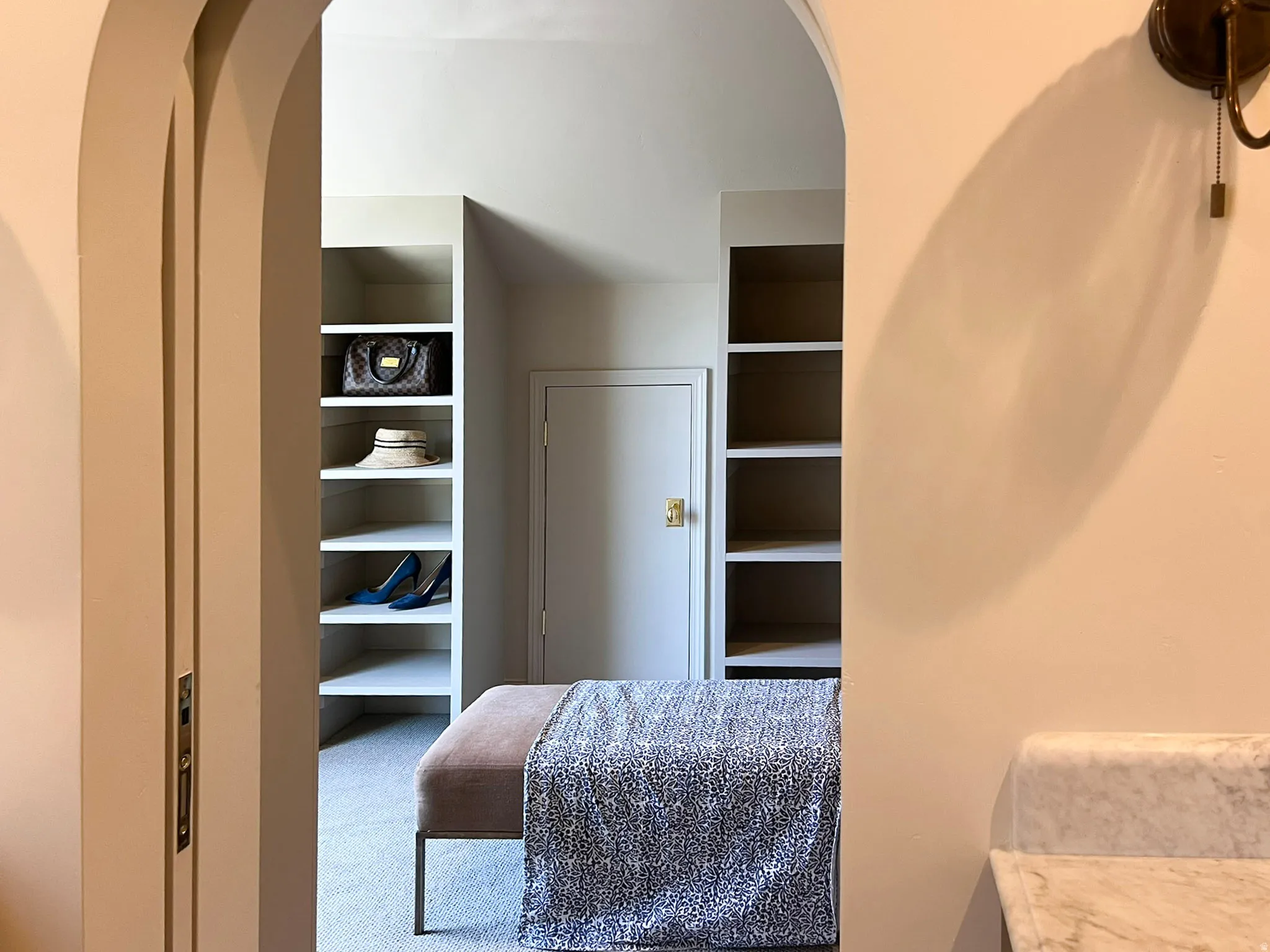 Arched entryway revealing built-in shelving, a neutral-toned door with brass hardware, and a marble countertop feature