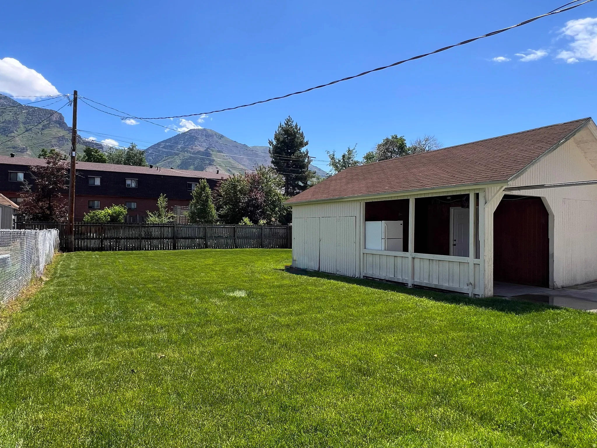Expansive green lawn with a detached outbuilding featuring white siding and a brown shingled roof, a covered porch, and mountains in the background