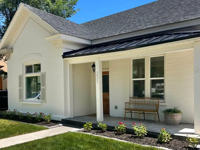 White painted brick exterior with a dark shingle roof, black metal awning, and a covered porch
