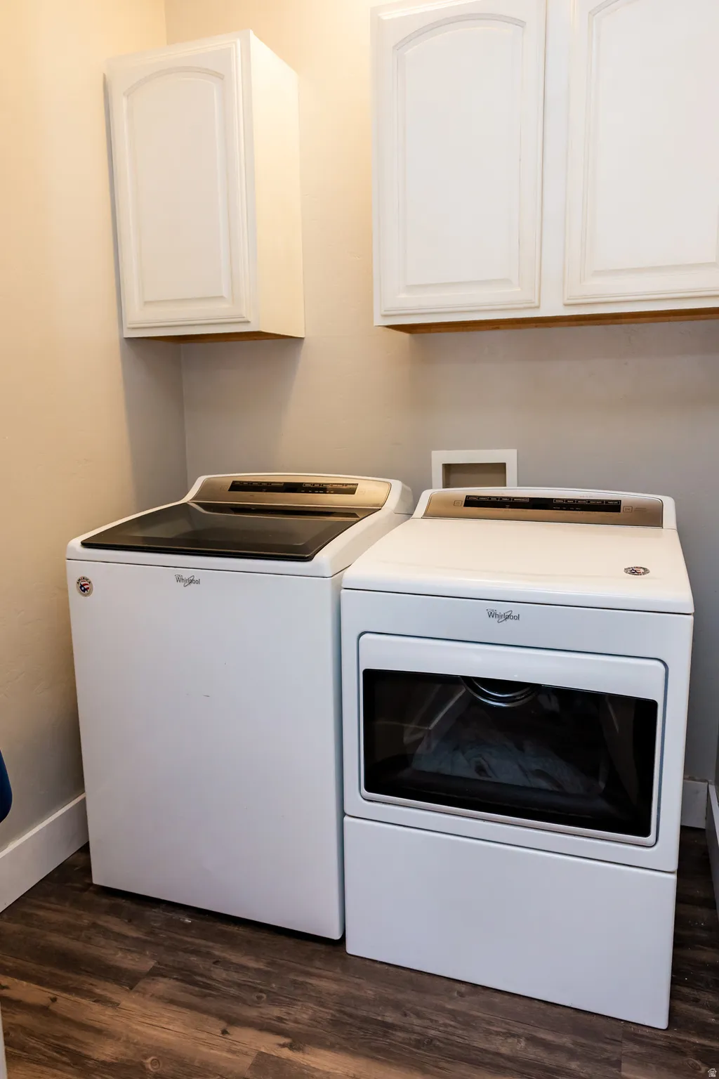 Dedicated laundry space featuring wood-finish flooring, light-toned walls, and white upper cabinetry with arch panel doors
