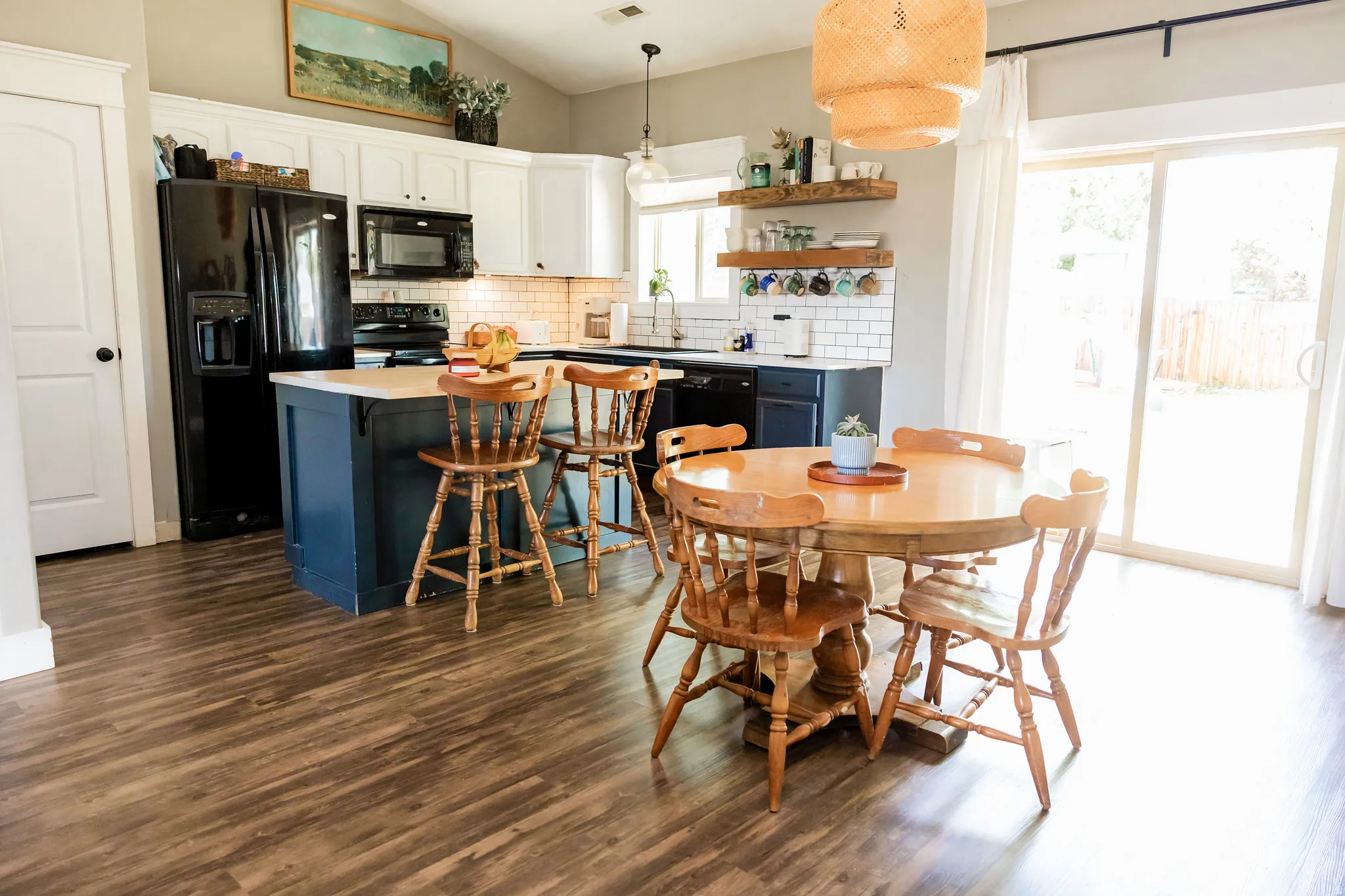 Kitchen featuring wood-finish flooring, a central island with countertop seating, white upper cabinetry, dark lower cabinetry, and subway tile backsplash
