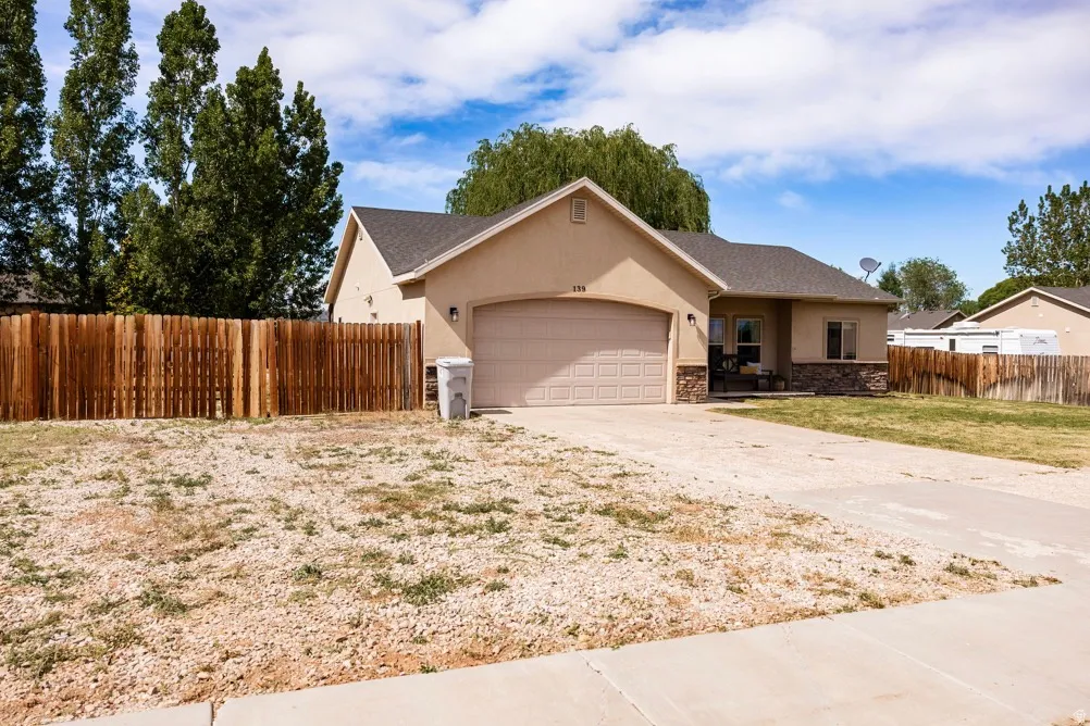 Exterior facade featuring stucco and stone accents, an attached garage, a covered front entry, and a wood privacy fence