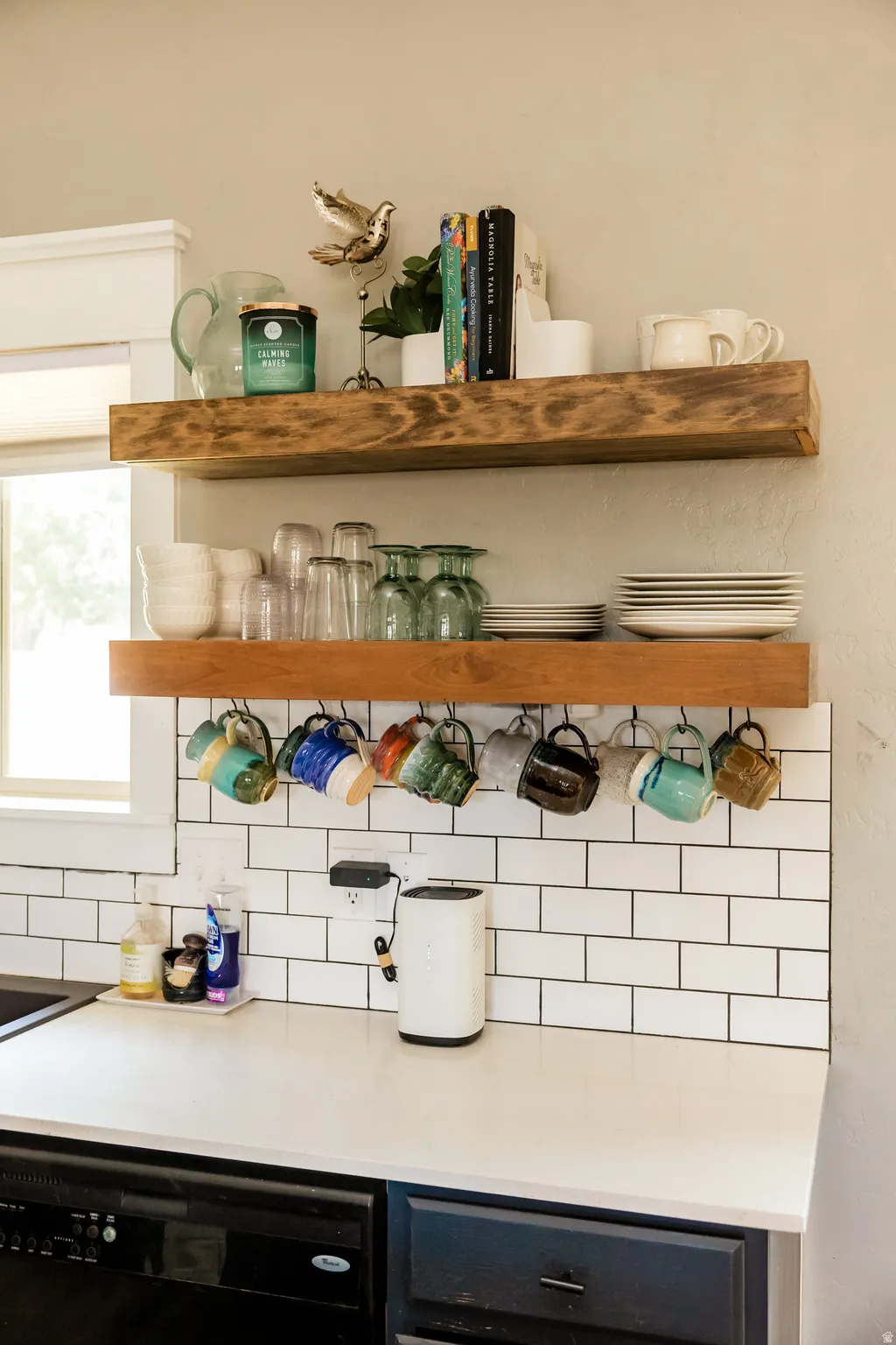 Kitchen featuring solid wood floating shelves, white subway tile backsplash, light-toned countertop, and integrated dishwasher
