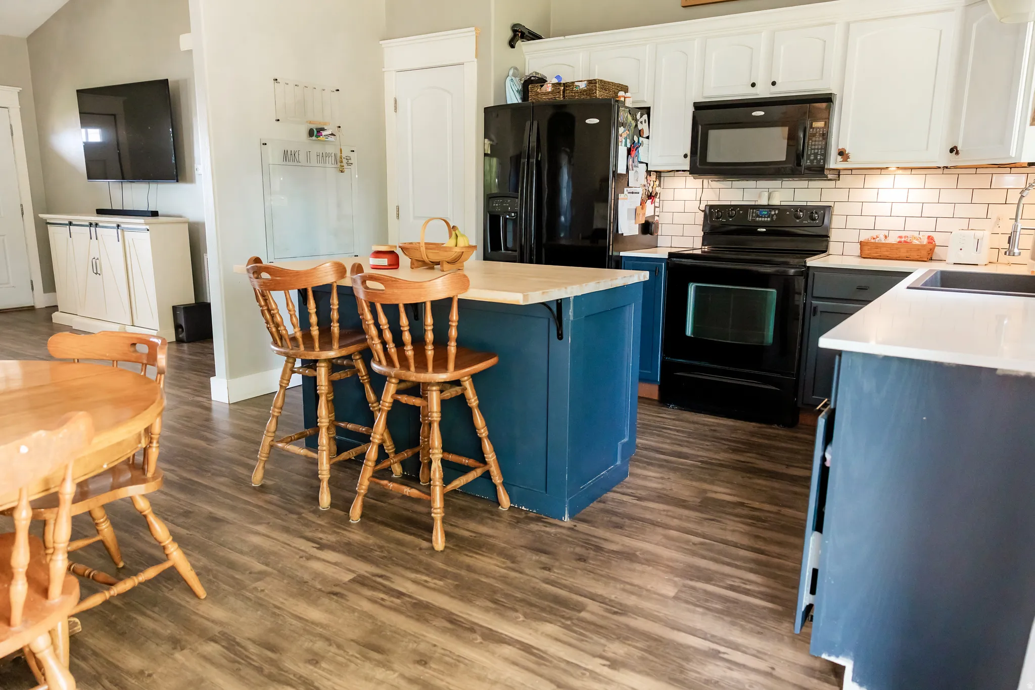 Spacious kitchen featuring wood-finish flooring, a blue island with a light-toned countertop, and white upper cabinetry
