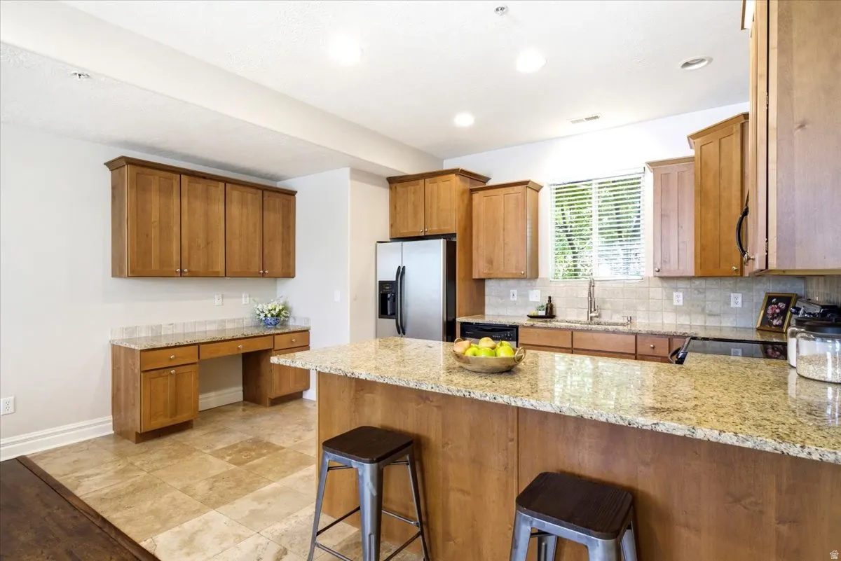 Kitchen featuring light wood cabinetry, stone-finish countertops, stainless steel appliances, and tile flooring