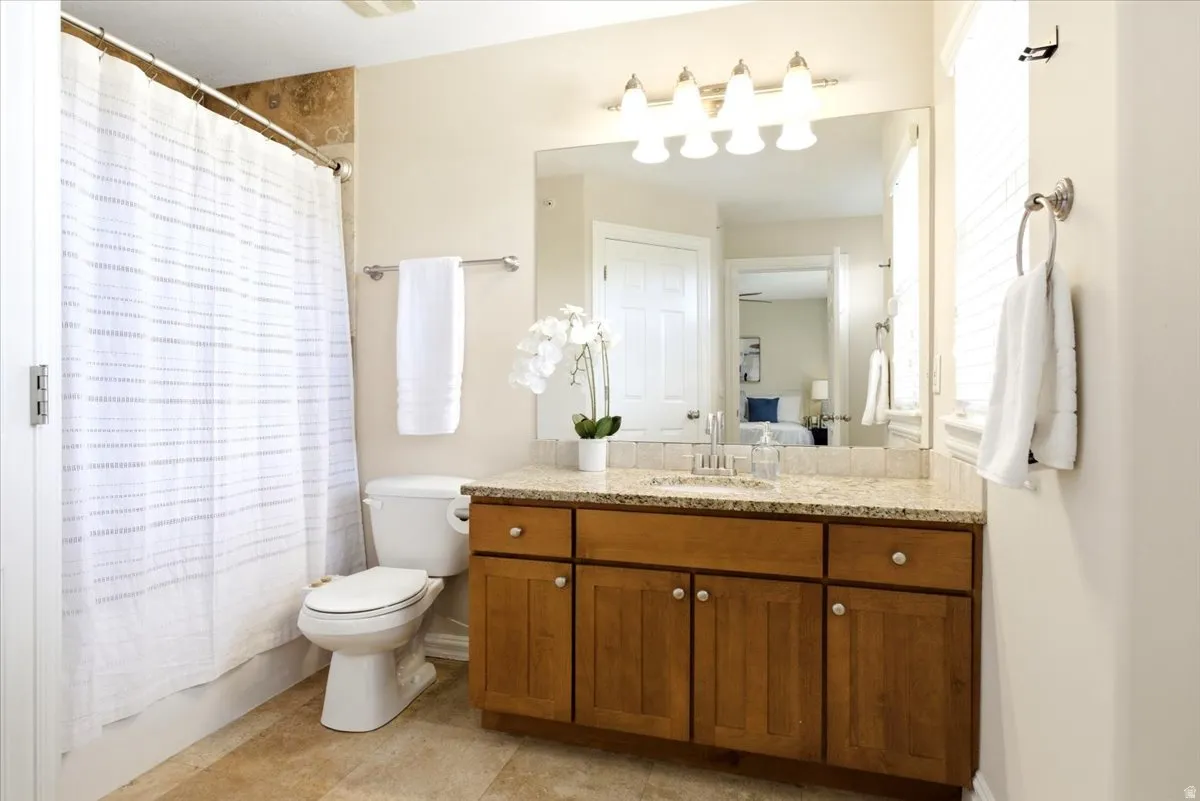Full bathroom featuring a wood-finish vanity with a light-toned countertop, a large wall mirror, and a five-light fixture