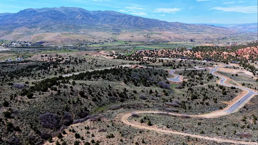 Expansive undeveloped land featuring a winding paved road, scattered natural vegetation, and distant mountainous terrain under a clear sky