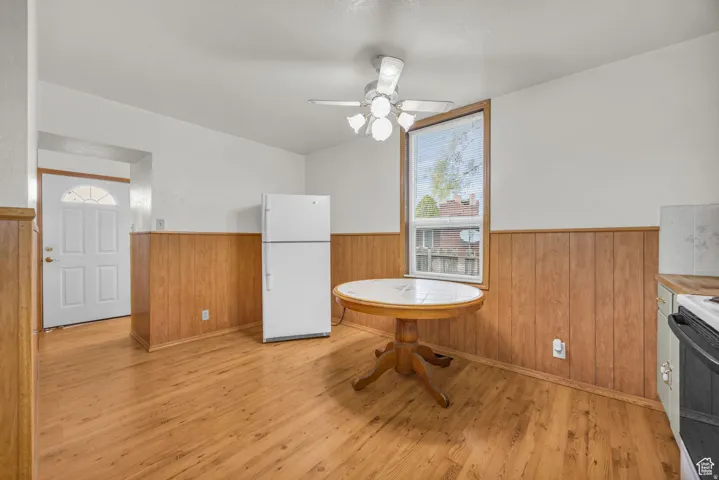 Well-lit eat-in kitchen area featuring wood-finish flooring, wood paneling, and a ceiling fan with integrated lighting