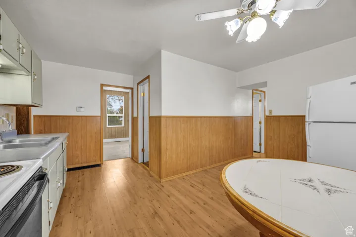 Kitchen space featuring wood-finish flooring, white walls with wood wainscoting, and a white ceiling fan with light fixture