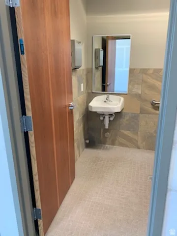 Restroom featuring a wall-mounted pedestal sink with a single-handle faucet, a rectangular mirror, and a grab bar