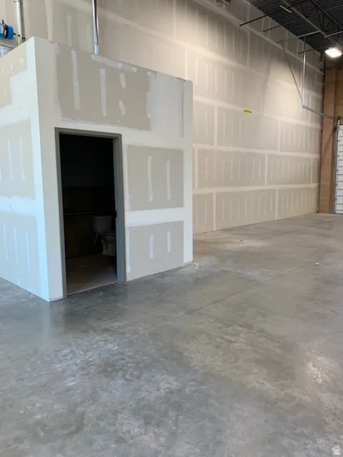 Expansive industrial space featuring a concrete floor, exposed ceiling joists, and a partially finished drywall enclosure