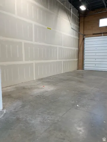 Spacious commercial interior featuring concrete flooring, unpainted drywall, exposed ceiling beams, and a roll-up garage door