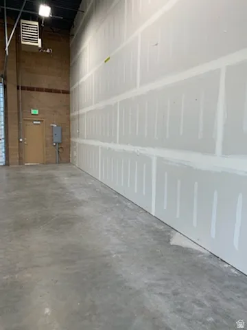 Expansive interior space featuring unfinished drywall, exposed ceiling joists, concrete flooring, brick wall accents, and an industrial-style heater