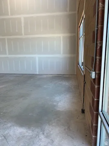 Interior space featuring unfinished drywall, concrete flooring, and an exterior brick wall with a window