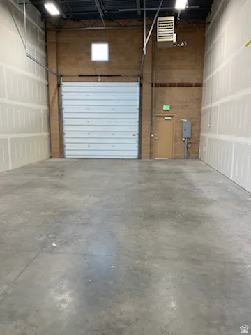 Spacious interior with a large roll-up door, polished concrete flooring, exposed ceiling joists, and fluorescent lighting