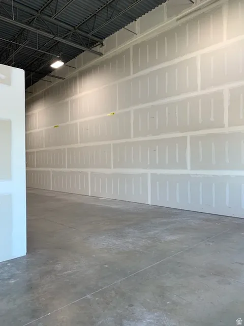 Expansive interior space featuring unfinished drywall, a concrete floor, and an exposed metal truss ceiling