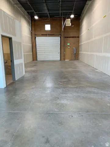 Spacious interior featuring a large roll-up door, exposed ceiling joists, concrete flooring, and unfinished drywall