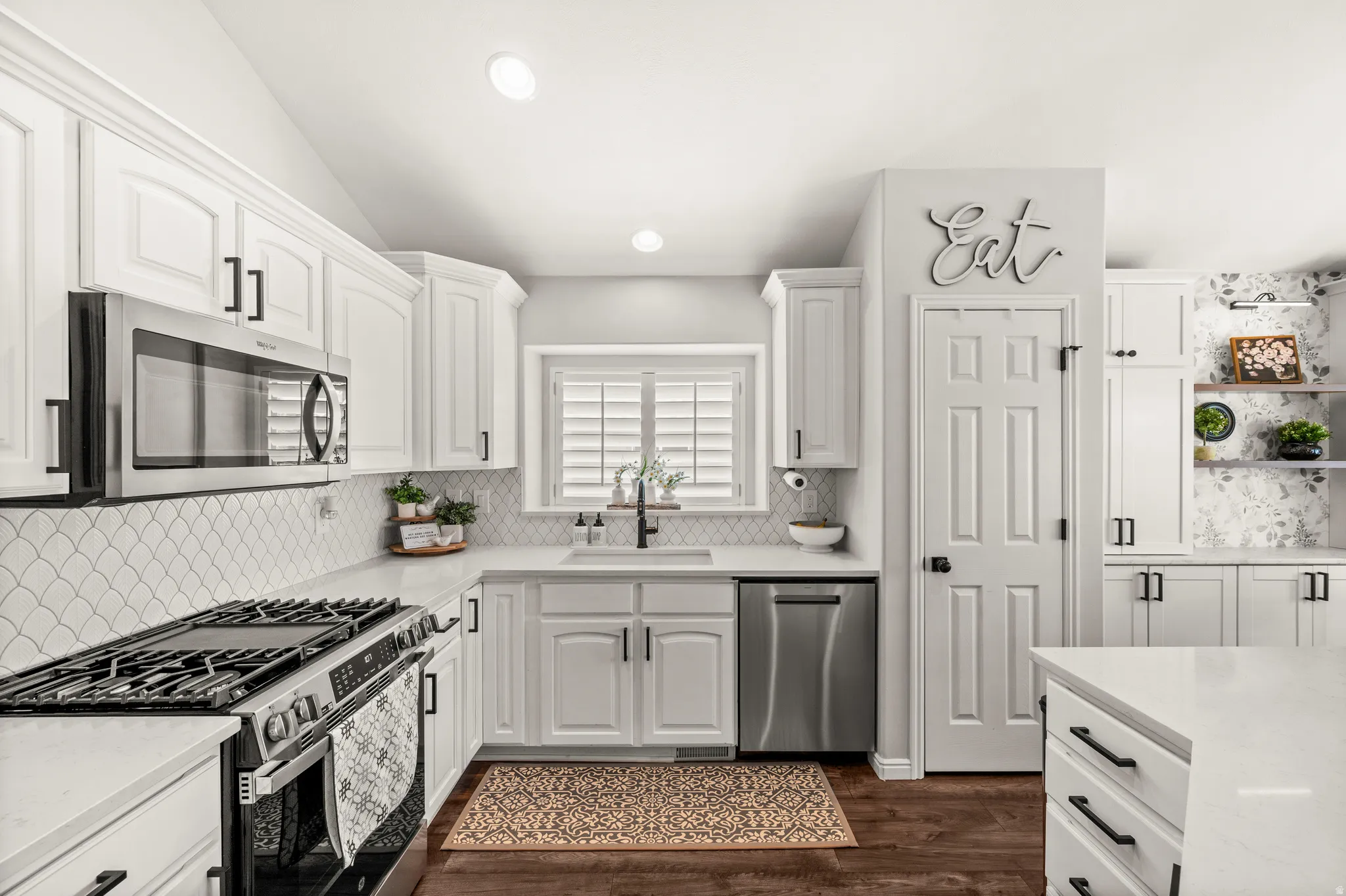 Modern kitchen featuring white cabinetry with dark hardware, stainless steel appliances, a gas range, and wood-finish flooring