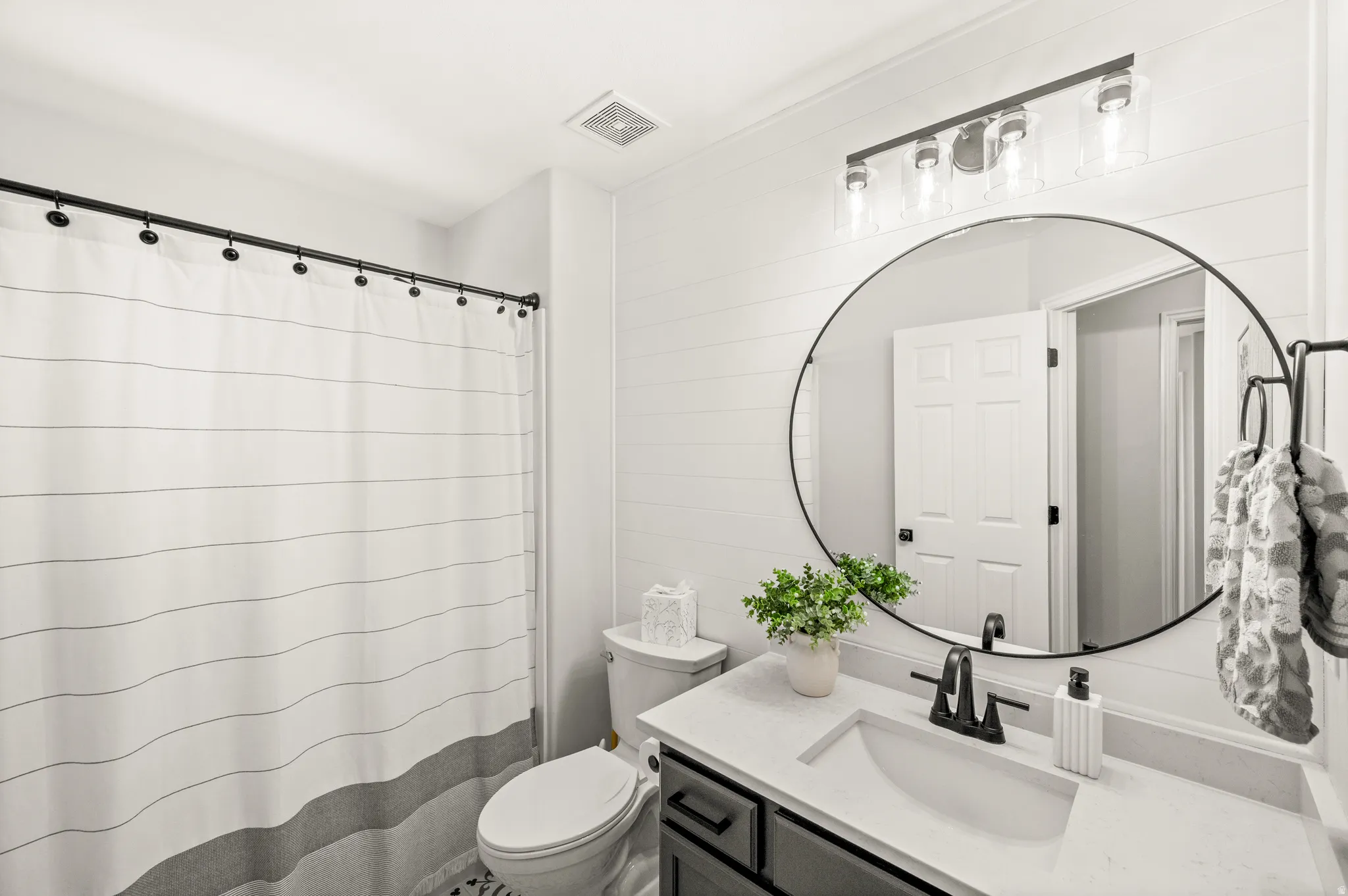 Bathroom featuring a dark gray vanity with a light countertop, a circular mirror, and a four-light fixture