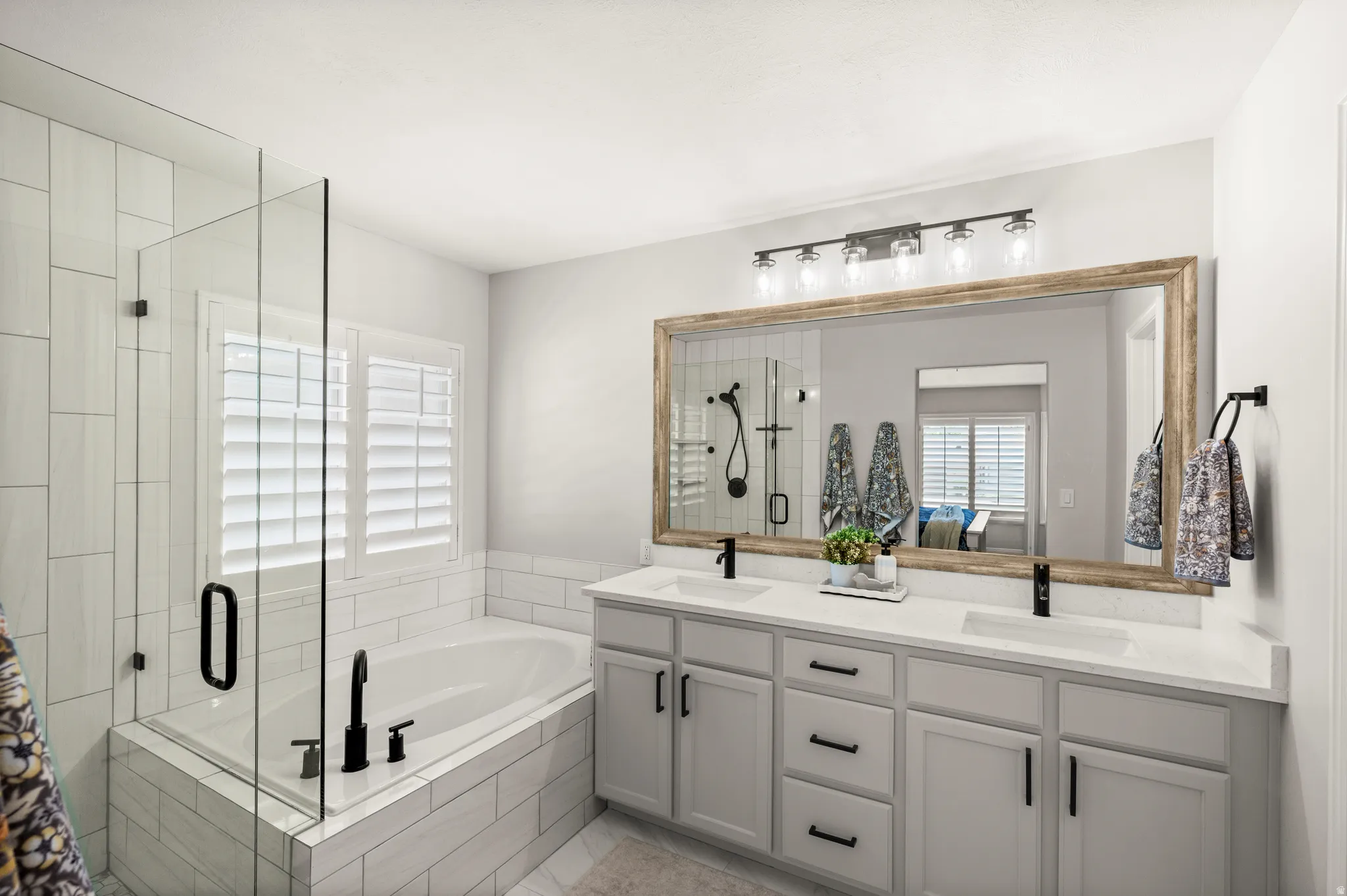 Spacious bathroom featuring a dual vanity with white countertops, a large framed mirror, and a five-light fixture
