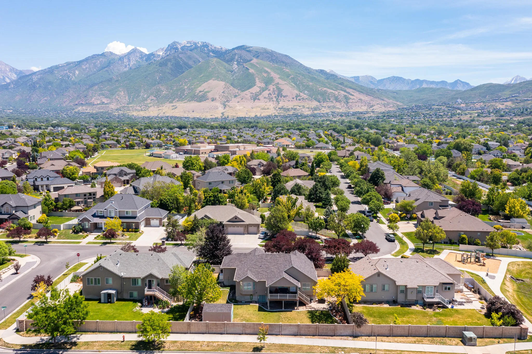Expansive aerial of a residential community featuring single-family homes, mature landscaping, and mountain backdrops