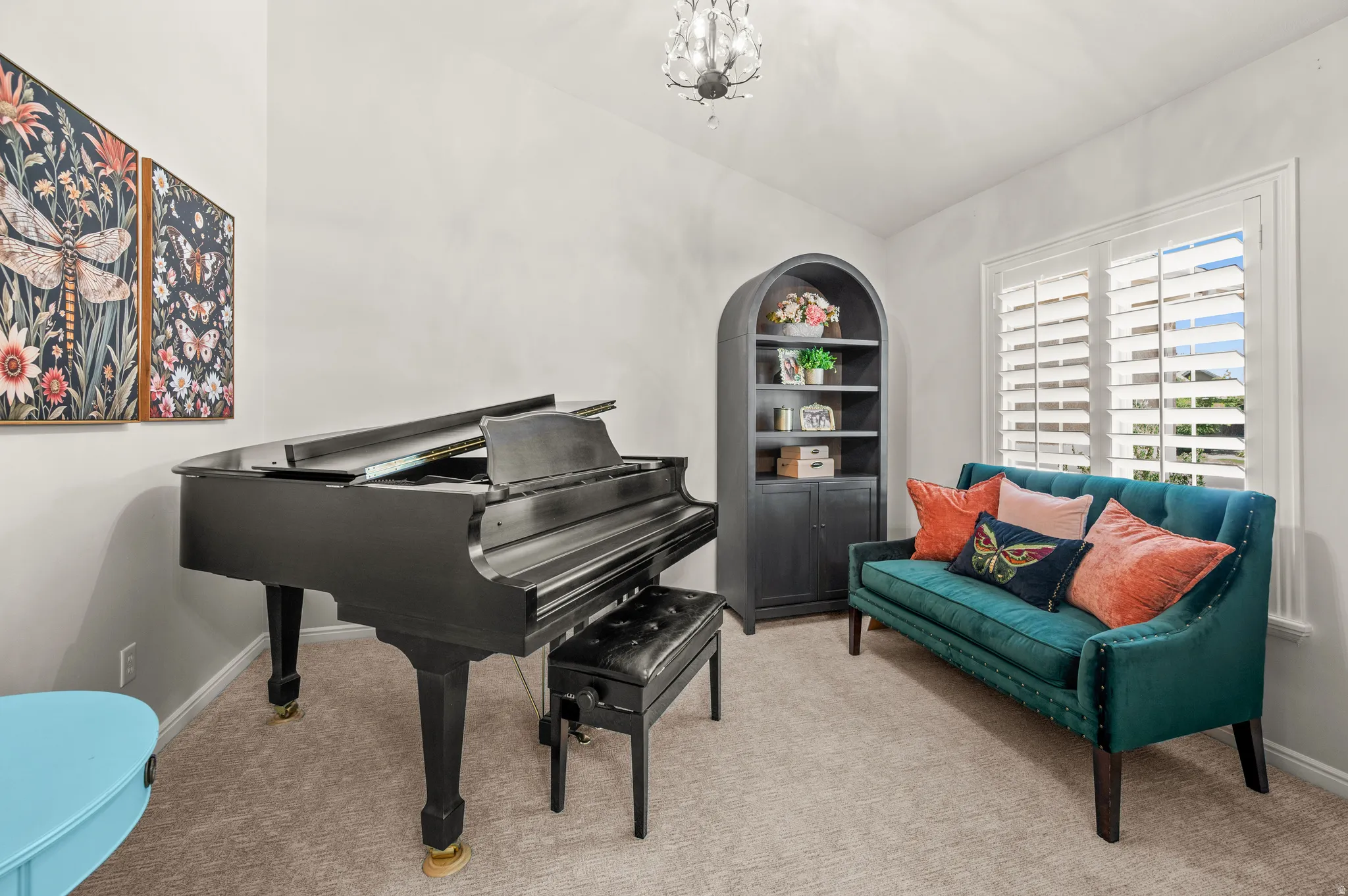 Carpeted room featuring a window with white plantation shutters, a dark arched bookshelf, and a decorative chandelier