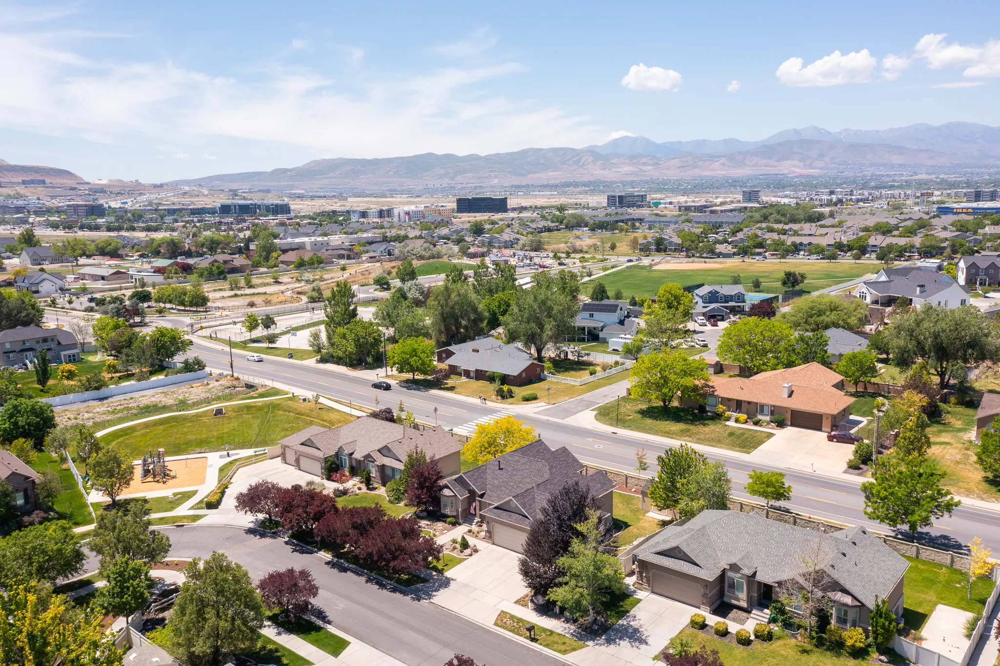Aerial perspective showcasing a residential neighborhood with diverse housing styles, mature trees, and a distant mountain range backdrop