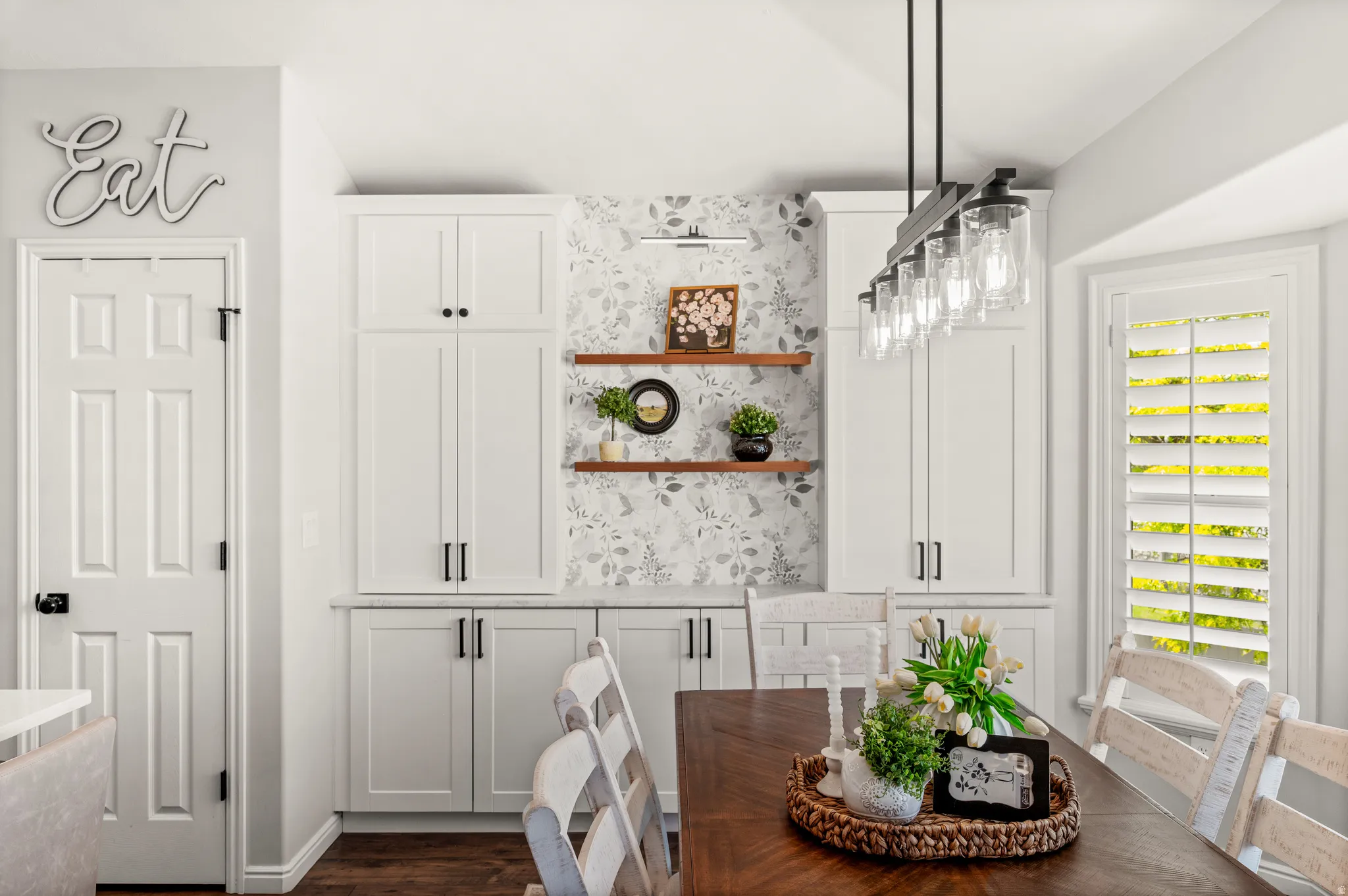 Dining area featuring custom built-in cabinetry with matte black hardware, floating wood shelves, and elegant botanical-patterned wallpaper