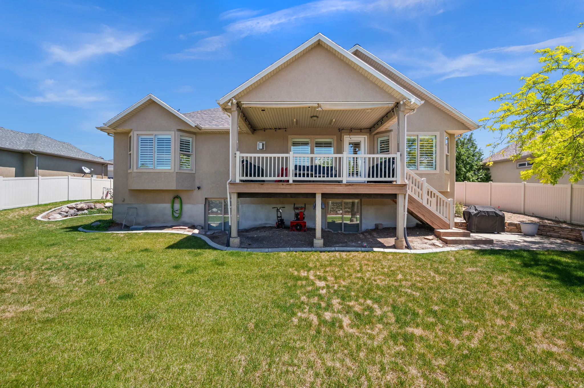 Expansive backyard featuring a manicured lawn, a raised deck with a covered patio, and a lower-level concrete patio
