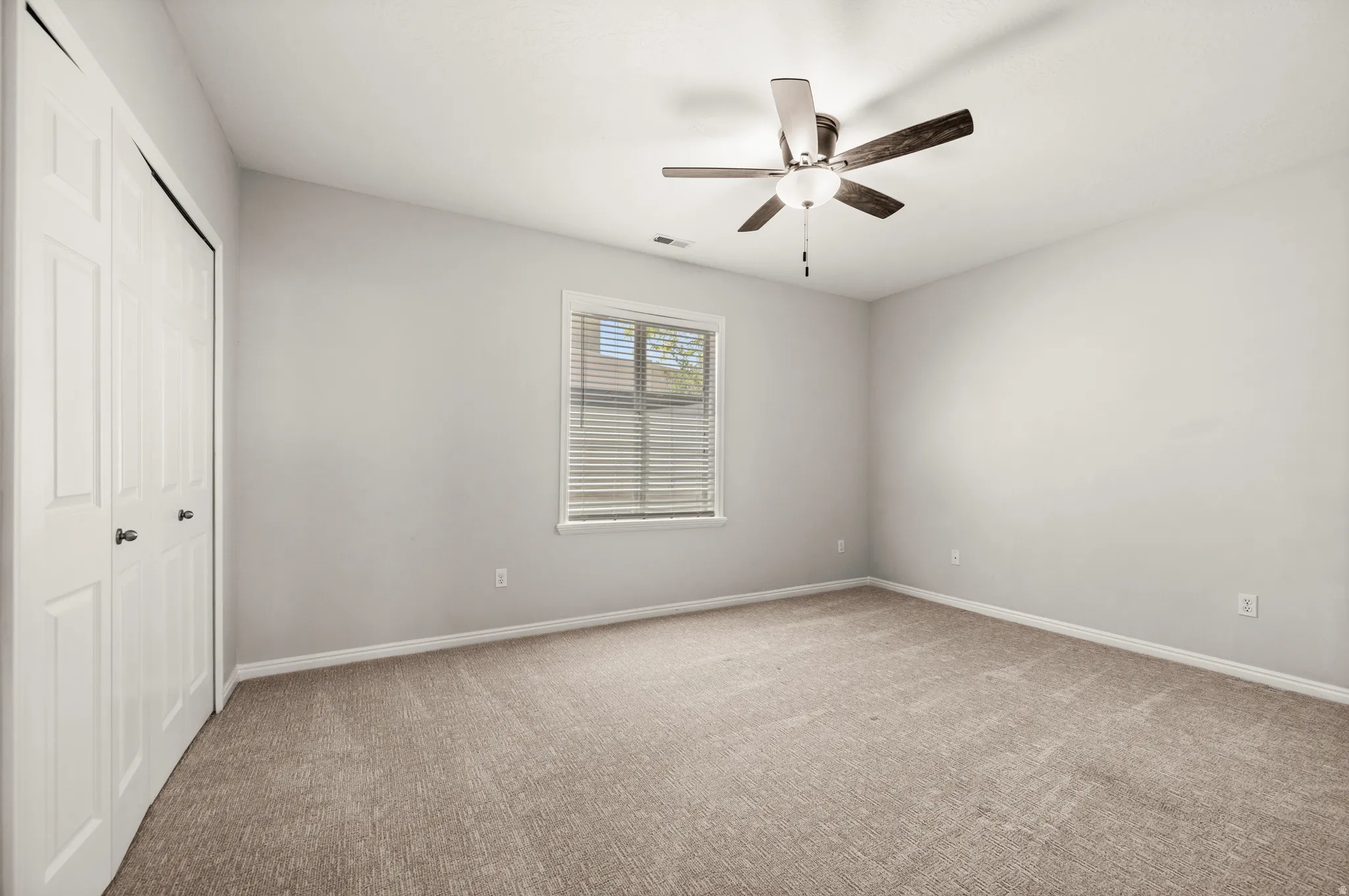 Carpeted room featuring a ceiling fan, white bi-fold closet doors, a window with horizontal blinds, and neutral wall tones