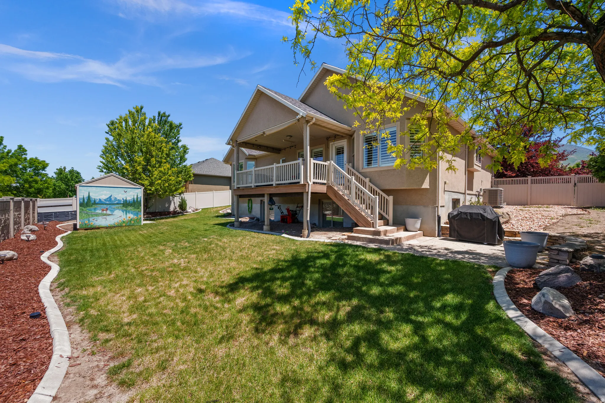 Expansive backyard featuring a manicured lawn, established trees, and a terraced patio area