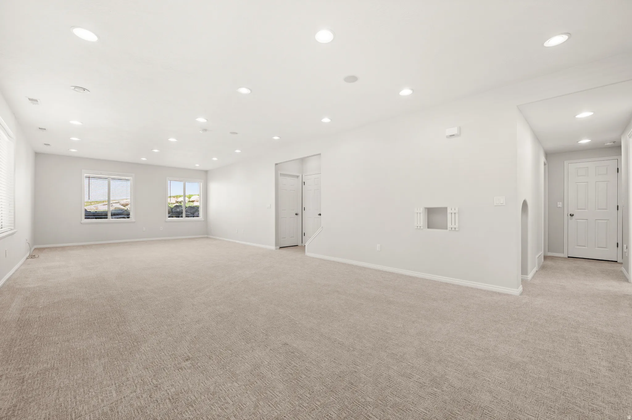 Spacious room featuring neutral carpeting, recessed lighting, and multiple windows providing natural light