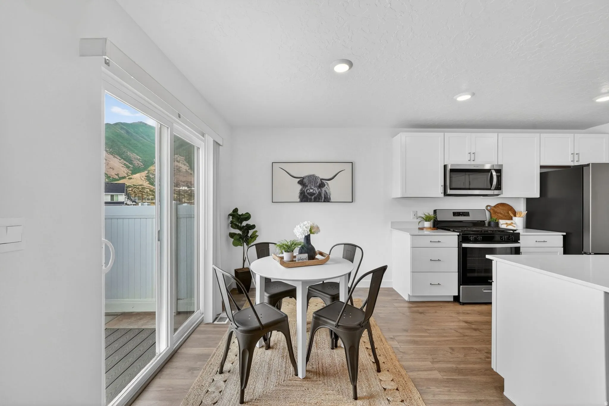 Open-concept kitchen and dining area featuring white cabinetry, stainless steel appliances, and wood-finish flooring