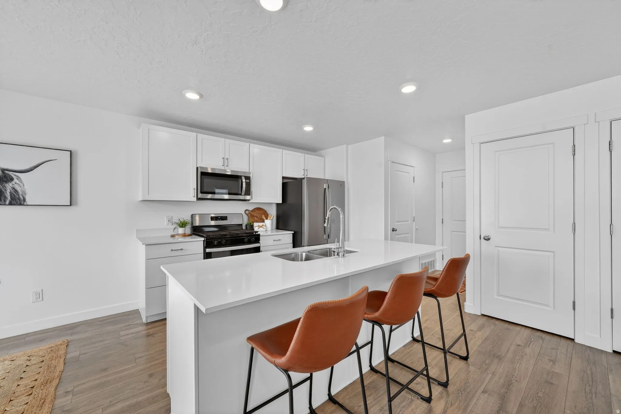 Modern kitchen featuring a large central island, white cabinetry with brushed nickel hardware, stainless steel appliances, and wood-finish flooring