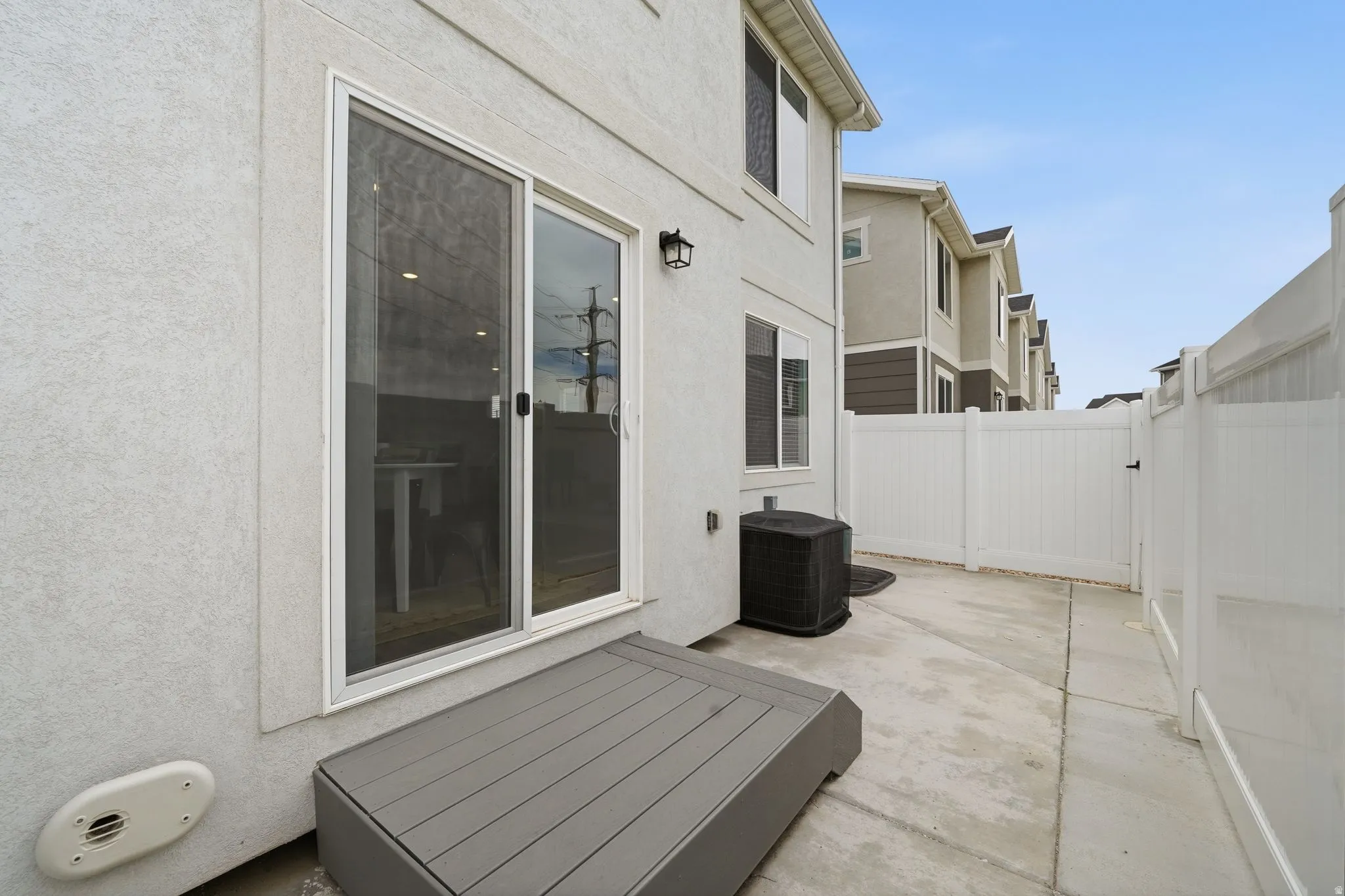 Private outdoor patio area featuring a white vinyl fence, concrete paving, and a grey composite step