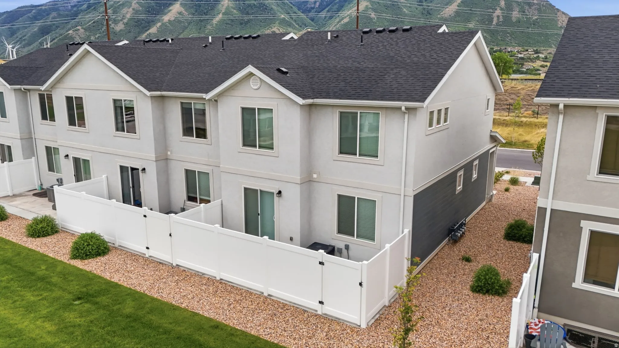 Rear exterior featuring a private fenced patio area, gravel landscaping, and mature shrubbery