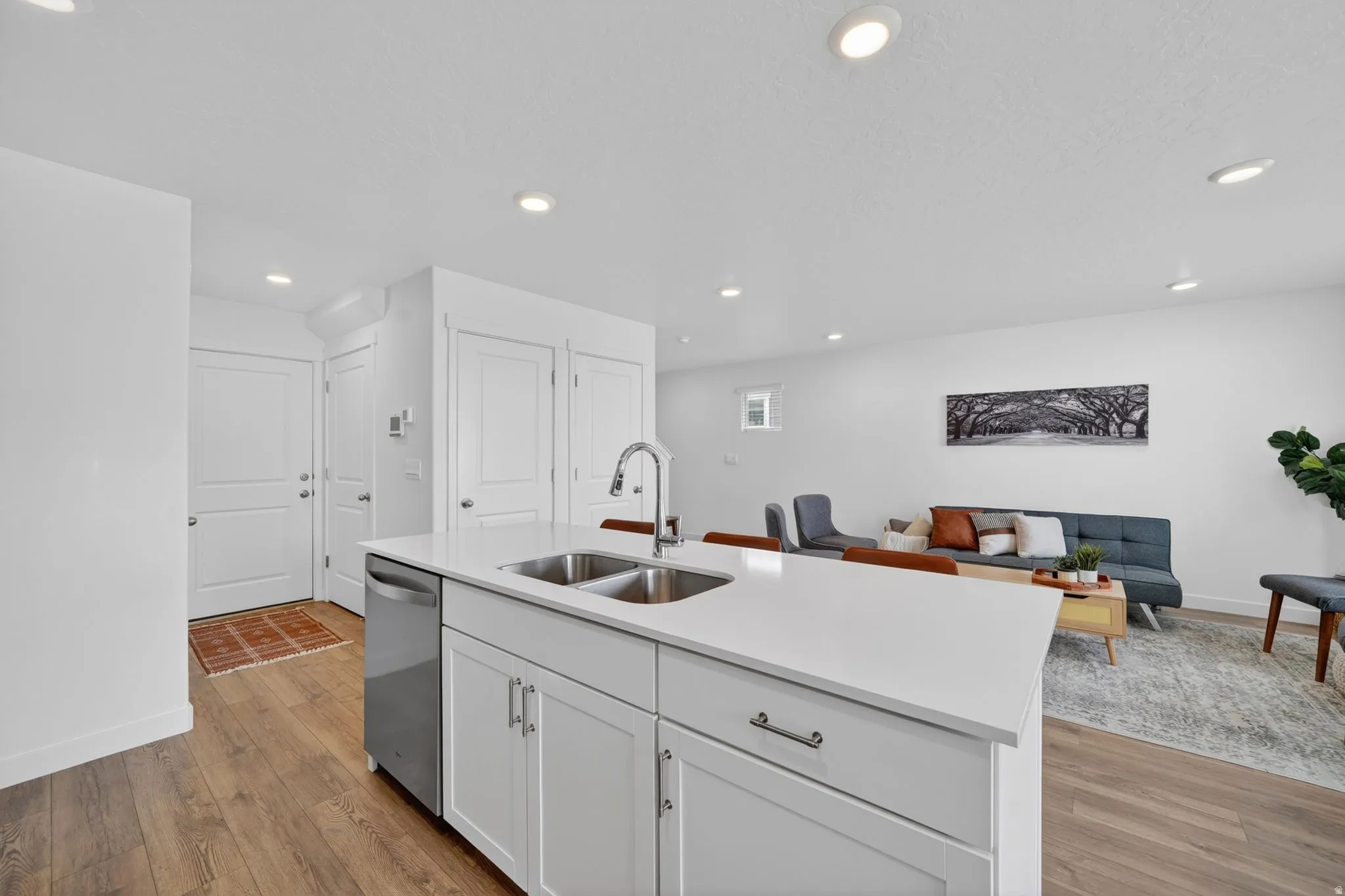 Open-concept living space featuring a kitchen island with white cabinetry and a stainless steel double sink, wood-finish flooring, recessed lighting, and white walls