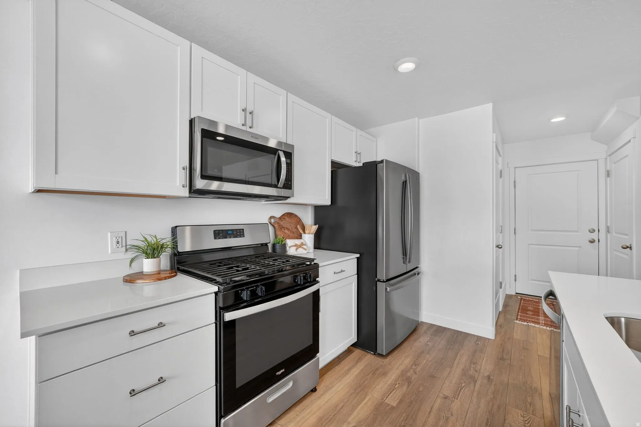 Modern kitchen featuring white shaker cabinetry, stainless steel appliances, light-toned countertops, and wood-finish flooring