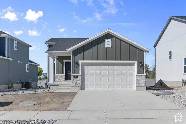 Exterior featuring vertical siding, masonry stone veneer, asphalt shingle roof, attached garage, and concrete driveway