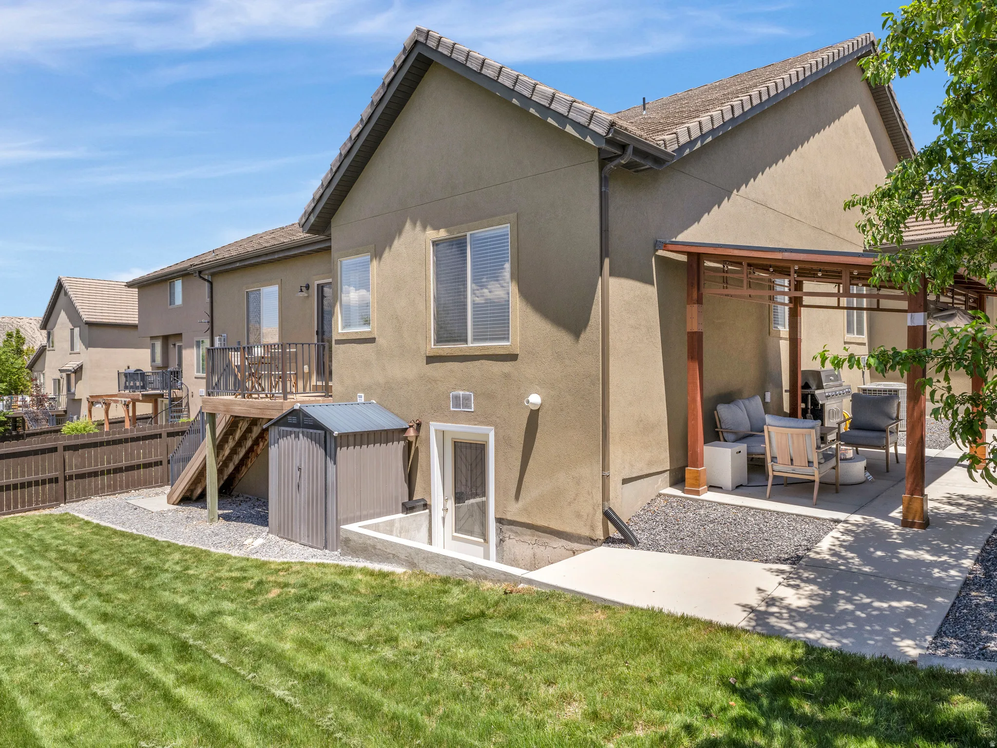 Expansive backyard featuring a manicured lawn, a raised wood deck with metal railings, and a concrete patio with a wood pergola