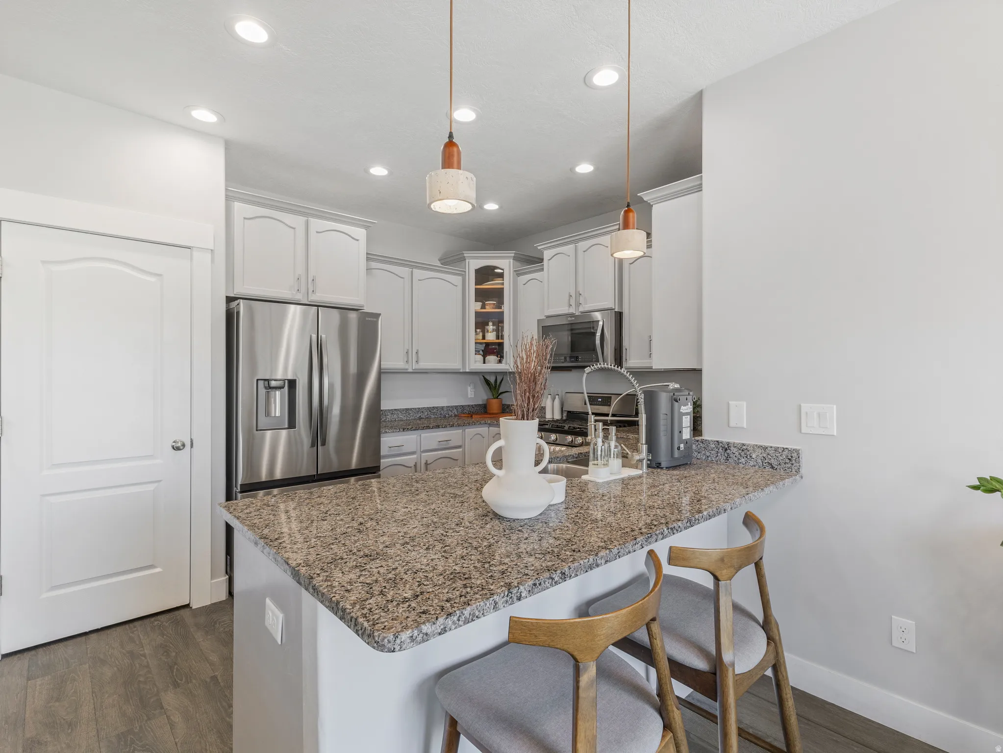 Kitchen island with granite countertop, stainless steel appliances, shaker-style cabinetry, recessed lighting, and wood-finish flooring