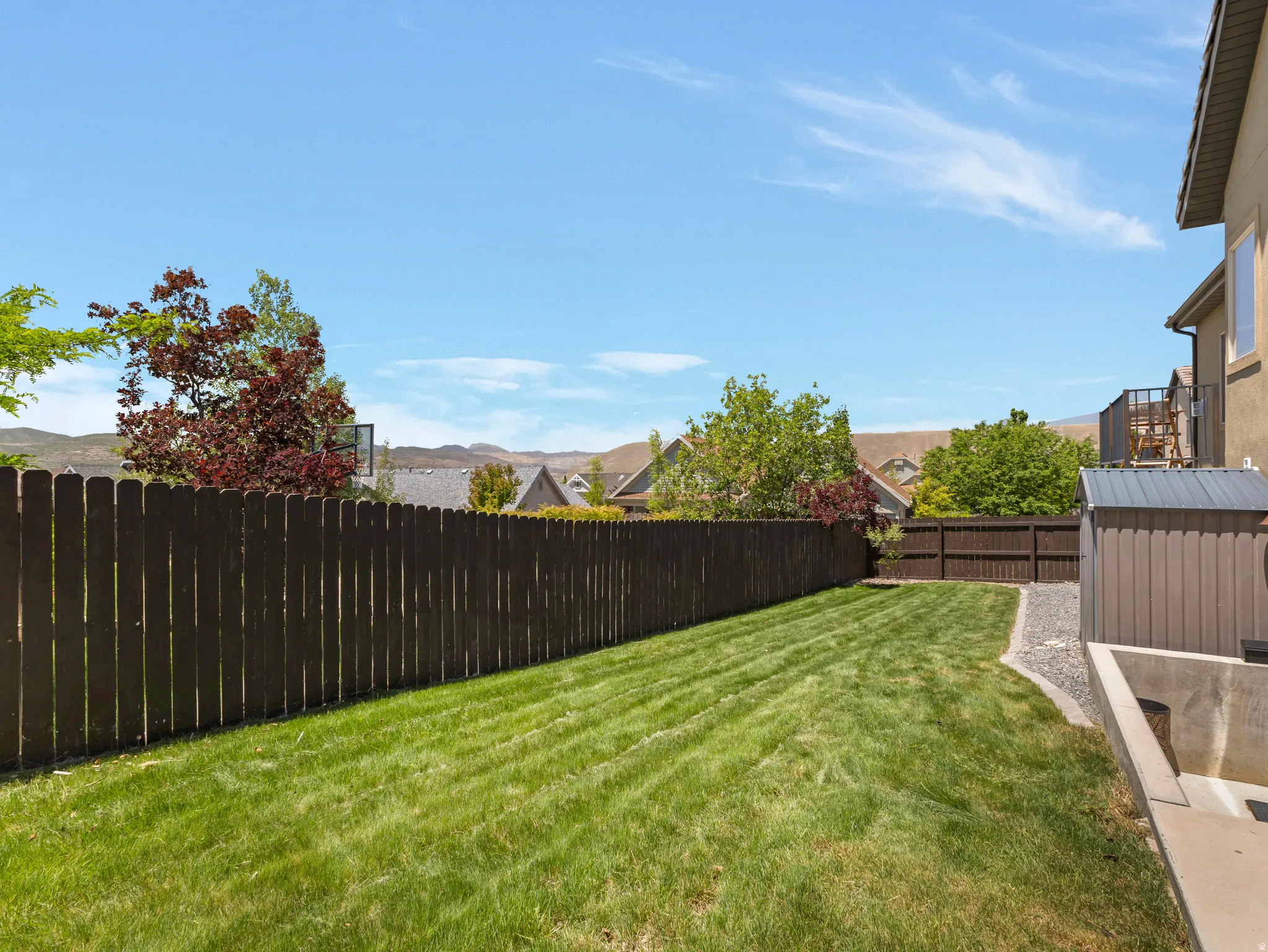 Expansive backyard featuring a manicured lawn, full privacy fence, and a storage shed